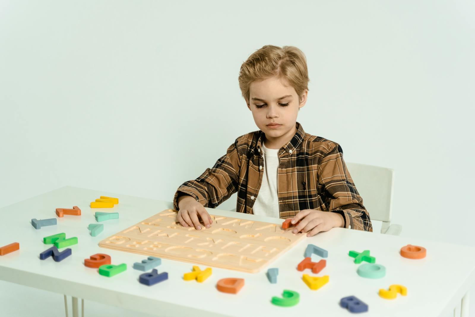 Ein Kind spielt mit bunten Alphabet-Lernspielzeugen am Tisch. Konzentriertes Lernen im häuslichen Umfeld.